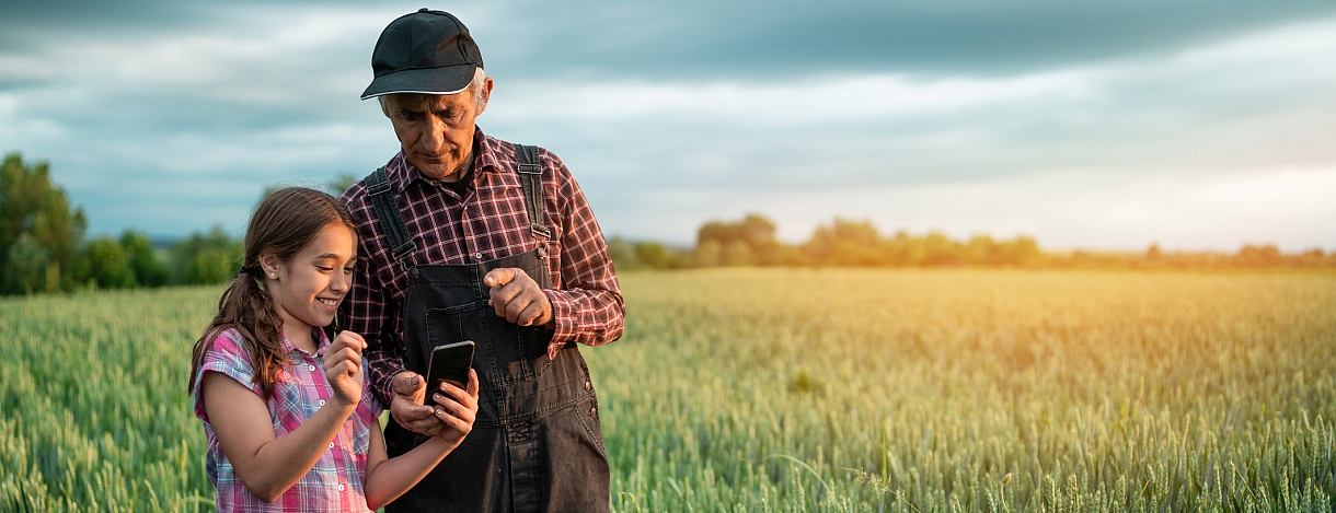 Landwirt und Enkeltochter mit Smartphone im Getreidefeld